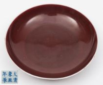 A Chinese sang-de-boeuf glazed saucer dish: the rim and underside of base glazed white,