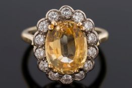 A yellow sapphire and diamond oval cluster ring: with central oval sapphire approximately 11.