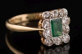 An emerald and diamond rectangular cluster ring: with central rectangular emerald within a border