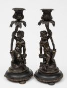 A pair of 19th century bronze figural candlesticks: depicting putti seated below flowering stems