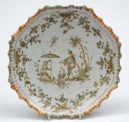 A French faience plate: of shaped form with cusped rim painted in green and yellow with a figure