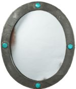 An Arts & Crafts period beaten pewter wall mirror: the oval mirror plate enclosed by a frame with