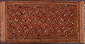 A Turkoman rug: the brick red field with three rows of stepped geometric stellar medallions,