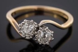 An 18ct gold and diamond two-stone cross over ring: with cushion-shaped old brilliant-cut diamonds