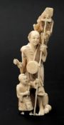 A Japanese carved ivory okimono of a street musician: with child and monkey, signed, 17cm. high.