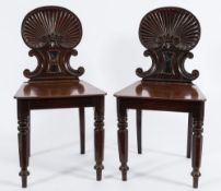 A pair of Regency carved mahogany hall chairs:, with reeded shell and scroll backs,