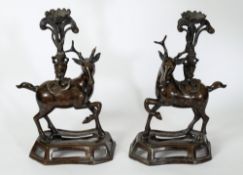 A pair of Chinese bronze deer stands: with inset eyes and mottled patination supporting vases of