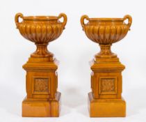 A pair of Victorian majolica ochre glazed twin-handled urns: of campana shape on square plinths,
