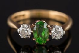 A demantoid garnet and diamond three stone ring: the central oval demantoid garnet approximately