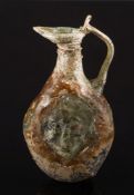 A Roman mould-blown olive green glass flask: of flattened form with a mask head to each side and