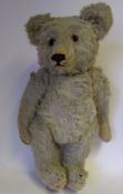A pale plush teddy bear: with rounded wide-apart ears, glass eyes and stitched snout,