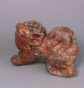 An Oriental carved hardstone lion dog: the stone of mottled grey, cream and russet colour,