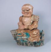 A Japanese decorated stoneware figure of a seated man: with grotesque frowning face,