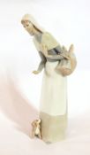 A Lladro figure of a woman wearing a wimple, carrying a basket of bread with a puppy at her feet,