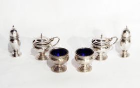 A George V silver cruet set comprising two open salts with blue glass liners,