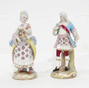A pair of continental figures of a gentleman dressed in a blue frock coat and his lady in floral