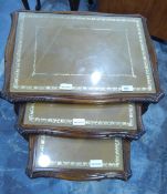 A nest of three mahogany tables inset tooled leather and glass covered topped and on slender