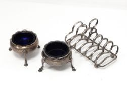 A pair of Georgian silver circular salts on three legs and a silver six-division toast rack,