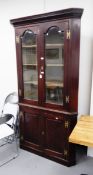 A mahogany double-breasted corner cabinet with glazed front opening to reveal serpentine shelves