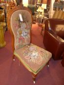 A late Victorian walnut nursing chair upholstered with needlepoint decorated with flowers.