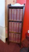 An oak open bookcase containing fifteen leather bound Charles Dickens novels