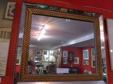 A contemporary designer mirror with rectangular plate and gold lattice frame.