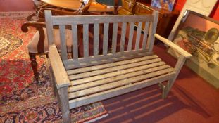 A weathered teak two seater garden bench of slatted construction