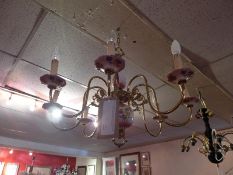 A brass Dutch style eight branch chandelier with ceramic detail decorated with flowers.