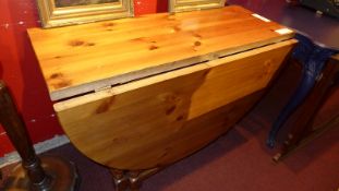 A solid pine drop flap dining table with oval flaps and raised on turned gateley supports.