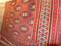 A Persian Bokhara rug the rouge ground having repeating gul motifs within a multi border.