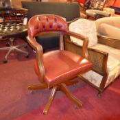 A desk chair upholstered in red leather and raised on swivel supports and castors.