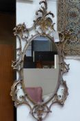A George III design giltwood wall mirror, the oval plate within ornately scrolled frame and