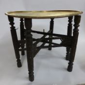 An Islamic Benares design brass tray table, the round decroated top over ornately carved hardwood