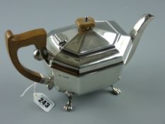 A silver teapot of oblong plain panelled form on four claw supports and with composition handle