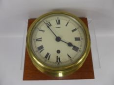 A Circular Brass Marine Clock, enamel face with Roman dial, mounted on an oak plinth, approx 17