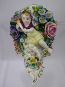 An Antique Sitzendorf Wall Mount, depicting a cherub carrying a torch surrounded by raised profuse