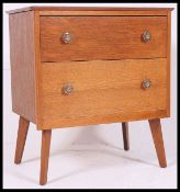 A vintage 1950's post war 2 drawer chest of drawers being raised on angled legs with brass handles.