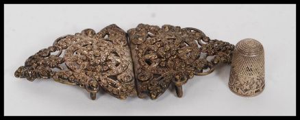 An ornate white metal nurses buckle along with a Victorian cased silver hallmarked textured Thimble