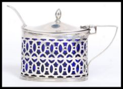 An early 20th century silver hallmarked fret worked mustard pot with hinged lid and blue glass