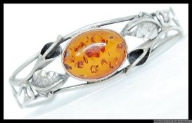 White metal bangle with stylised foliate pierced decoration with central cabachon amber style gem.
