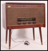 A vintage mid century teak radiogram having decorative facia panelling being raised on tapered legs.