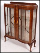 A 1930's walnut Queen Anne revival china display cabinet being raised on cabriole legs with glass