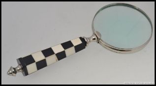 A large handheld magnifying glass with a checkerboard handle.