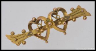 A 9ct gold early 20th century sweetheart brooch having intertwined hearts with filigree worked bar,