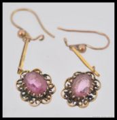 A pair of 9ct gold drop earrings having a central cut polished pink glass stone