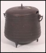 A 20th century rustic large cast iron cooking pot cauldron with lid raised on three legs