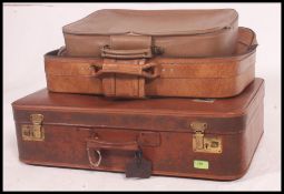 A stack of 3 20th century graduating suitcases to include 1950's vinyl covered examples, all brown.