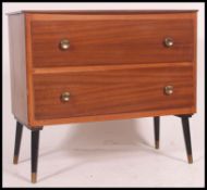 A 1950's retro teak wood chest of drawers being raised on tapered legs with 2 central drawers