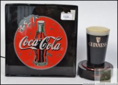 A retro shop advertising Coca Cola back lit electric sign along with a bar top Guinness advertising