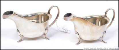 A pair of silver hallmarked creamers raised on splayed legs with hoop handles.